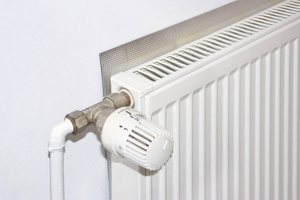 Ein weißer Heizkörper mit einem Thermostatventil, das manuell eingestellt werden kann, an einer weißen Wand montiert.