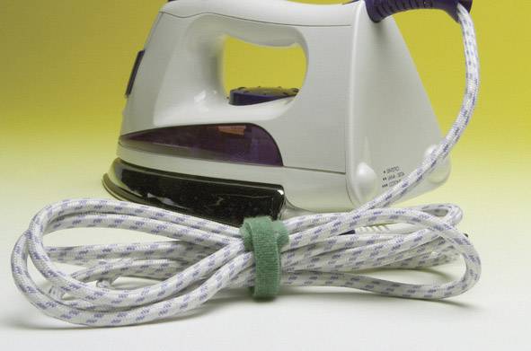 Ein weißes Bügeleisen mit lila Akzenten auf gelbem Hintergrund. Ein zusammengebundenes Kabel liegt vorne.