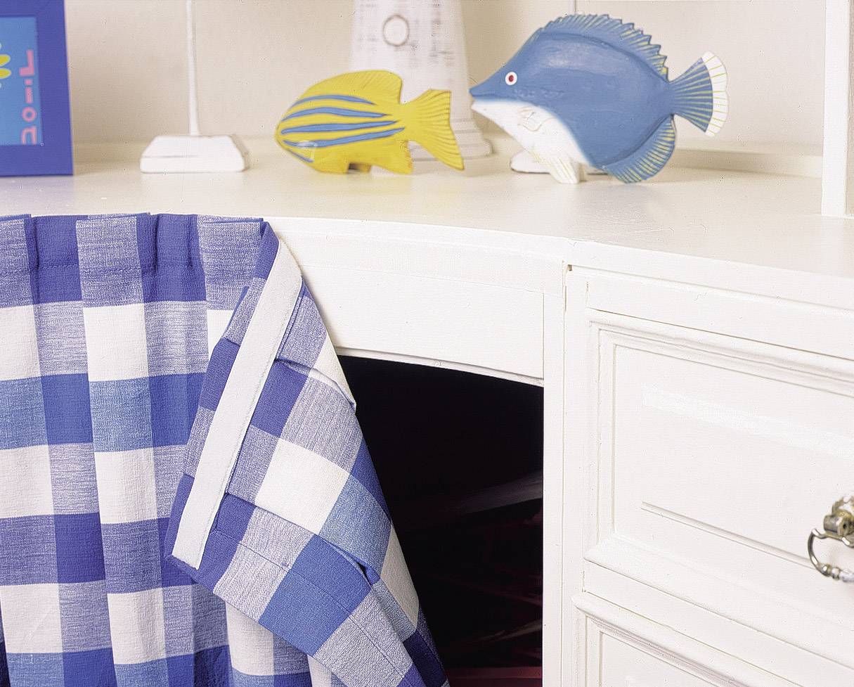 Weiße Kommode mit blau-weiß kariertem Tuch und zwei dekorativen Fischfiguren. Möbel und Deko setzen maritime Akzente.