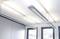 Beleuchtetes Büro mit modernen, weißen Pendelleuchten an der Decke und großen Fenstern, die viel Tageslicht hereinlassen.