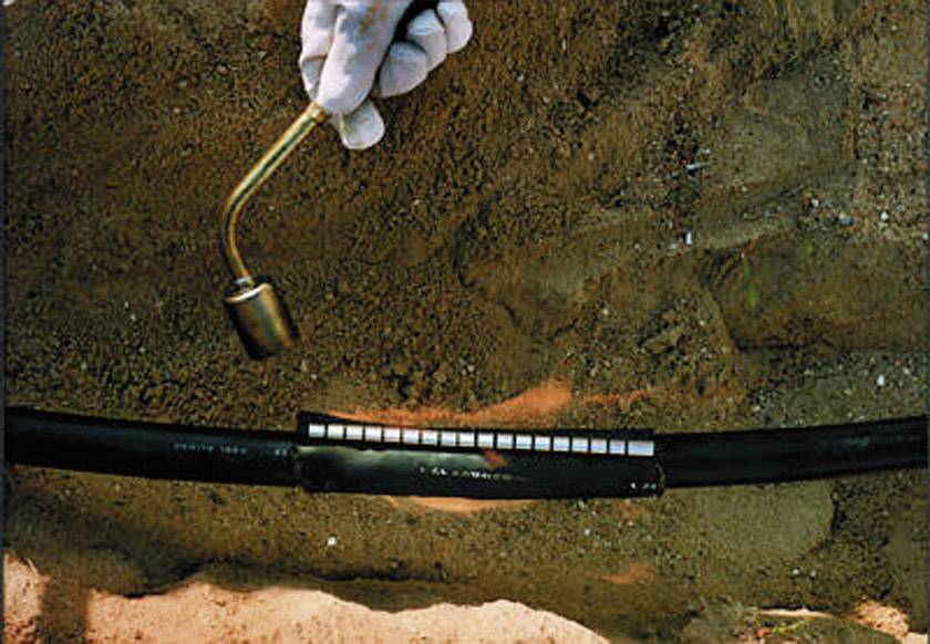 'Eine Person testet die Dichtheit einer unterirdischen Pipeline mit einem Hammer auf einer sandigen Oberfläche.'