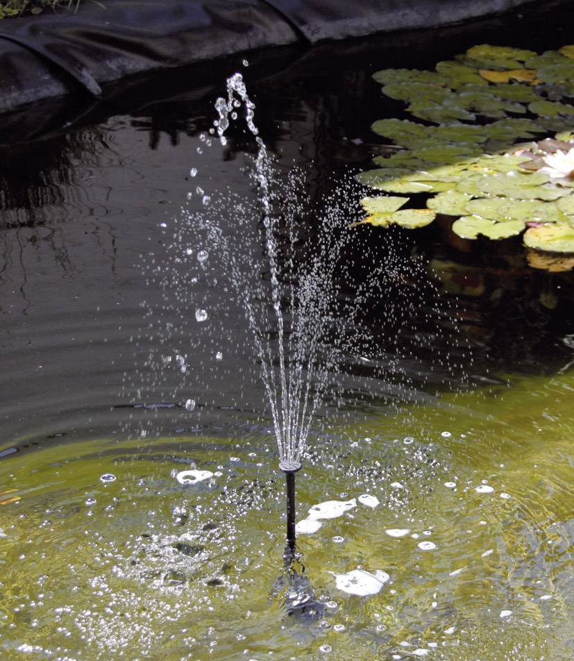 Ein kleiner Springbrunnen in einem Gartenteich, umgeben von Schwimmblättern, erzeugt sprudelnde Wasserstrahlen.