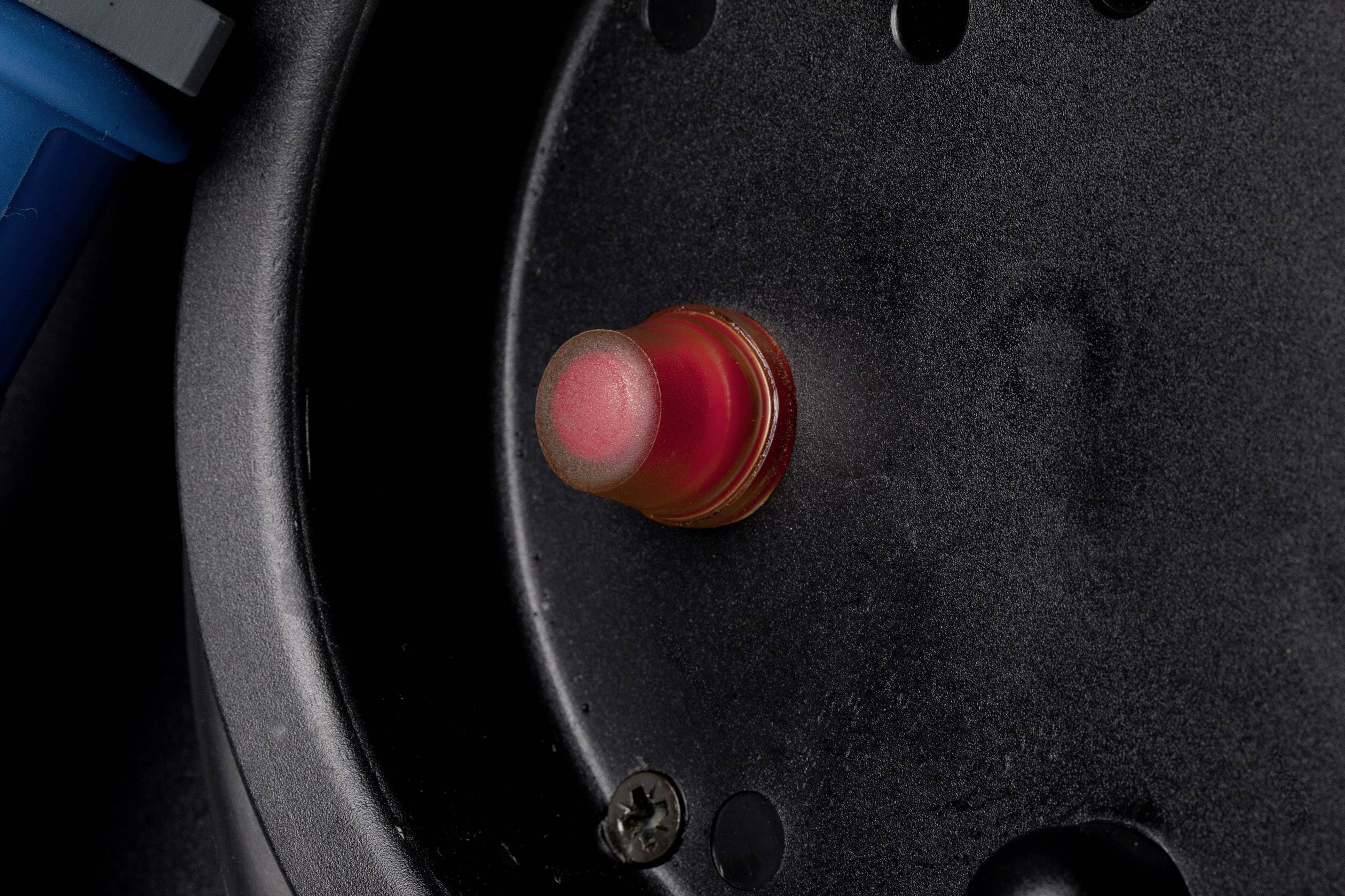 Ein roter Knopf auf einem schwarzen Gerät. Der Knopf ist hellrot hervorgehoben und scheint eine Funktion zu aktivieren.