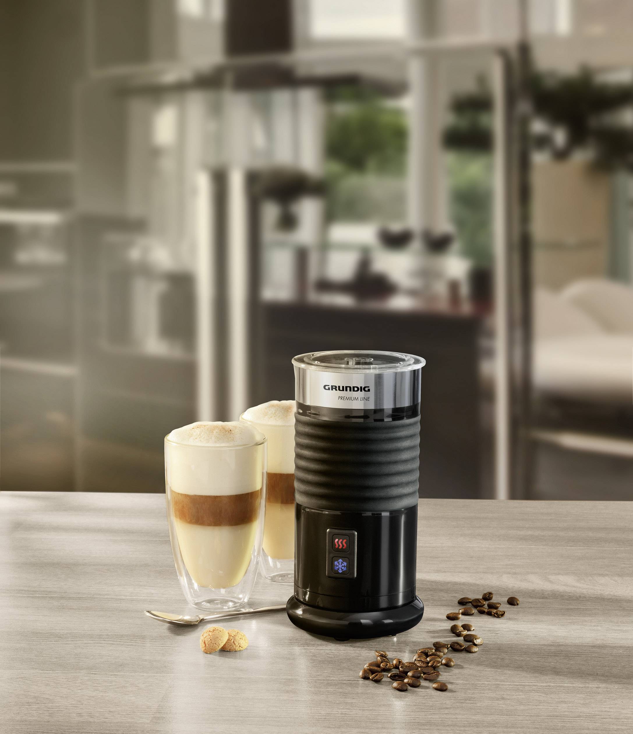 Elektrischer Milchaufschäumer auf der Arbeitsplatte mit zwei Gläsern Latte Macchiato, Kaffeebohnen verstreut. Modernes Küchenambiente.