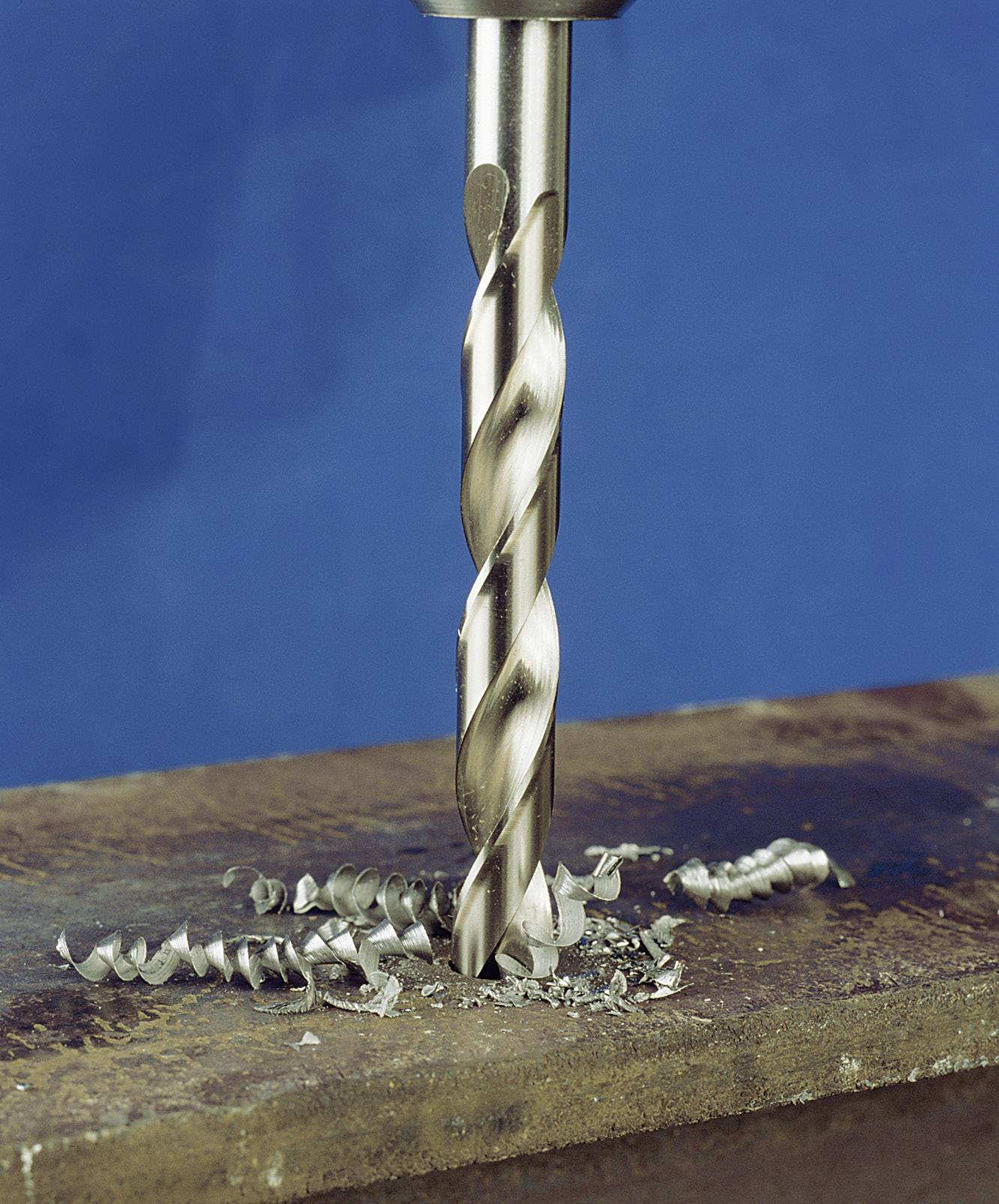 'Metallbohrer durchdringt Metallplatte, umgeben von Metallspänen, auf blauem Hintergrund.'