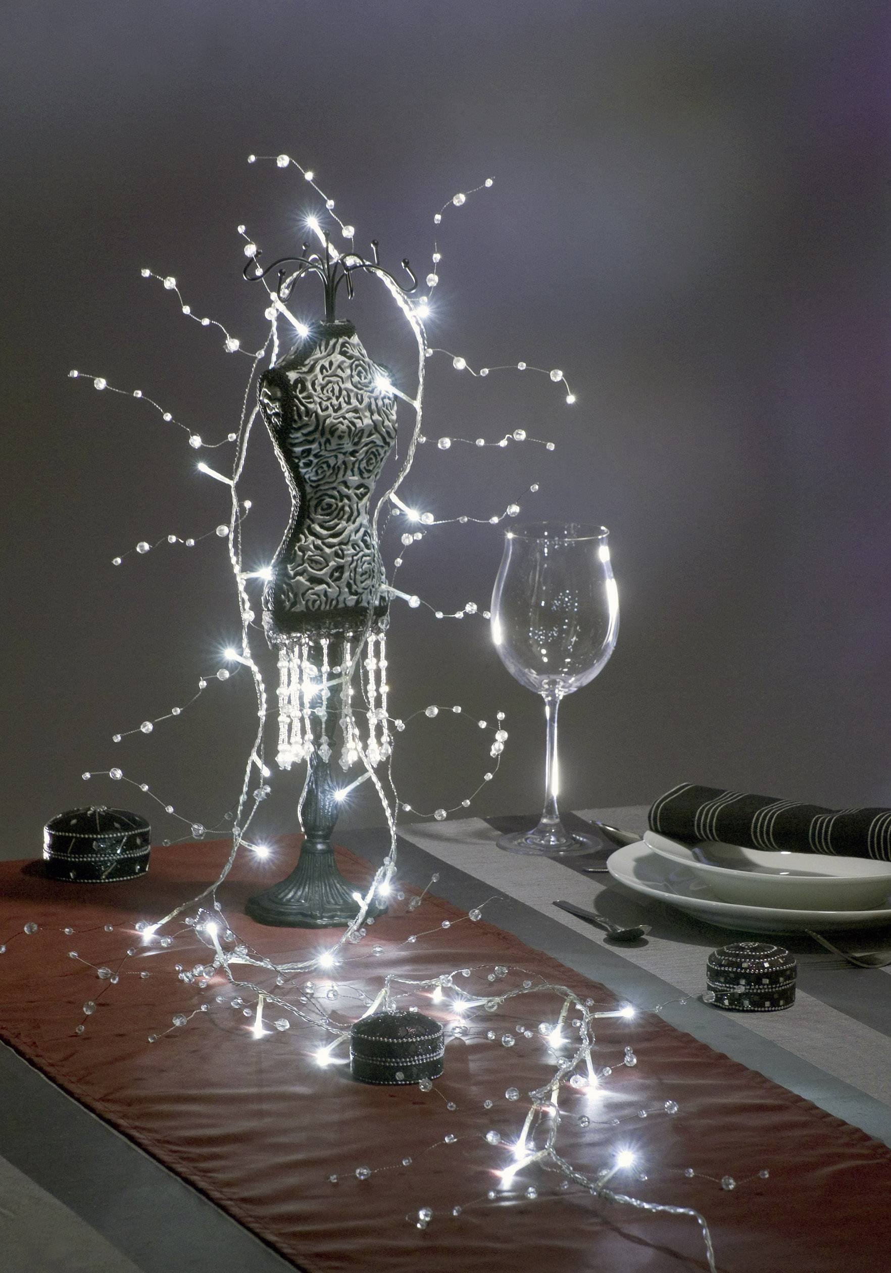 Ein dekorativer dunkler Tisch mit einem verzierten Schaufensterpuppe-Modell, umgeben von Lichterketten und neben einem Weinglas.