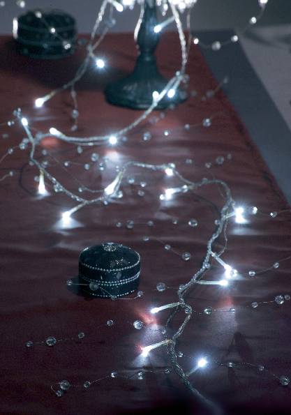 Ein dunkler Tisch ist mit einem roten Tuch bedeckt. Darauf liegen leuchtende Lichterketten und eine kleine, verzierte schwarze Schachtel.