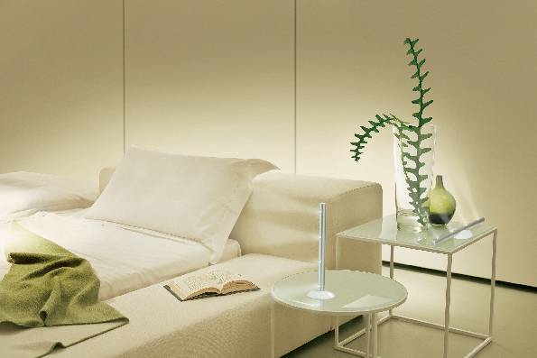 Ein modernes Schlafzimmer mit beigen Möbeln, einem aufgeschlagenen Buch, grünem Tuch und Pflanze auf einem Tisch. Minimalistisches Design.