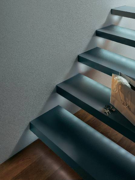 Eine moderne, schwebende Treppe mit Stufen aus Glas, beleuchtet durch Fensterlicht, daneben eine Tasche auf dem Geländer.