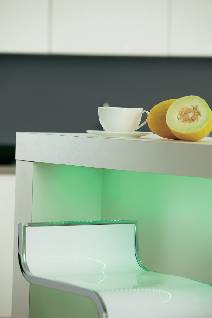 Heller moderner Küchenbereich mit Neonlicht. Auf der Bartheke stehen eine Tasse und aufgeschnittene Melonen. Ein Barhocker davor.
