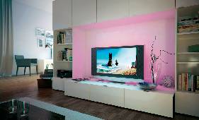 Ein modernes Wohnzimmer mit einem Flachbildfernseher in der Mitte. Links stehen Bücherregale und oben Fotos. Warmes Umgebungslicht.