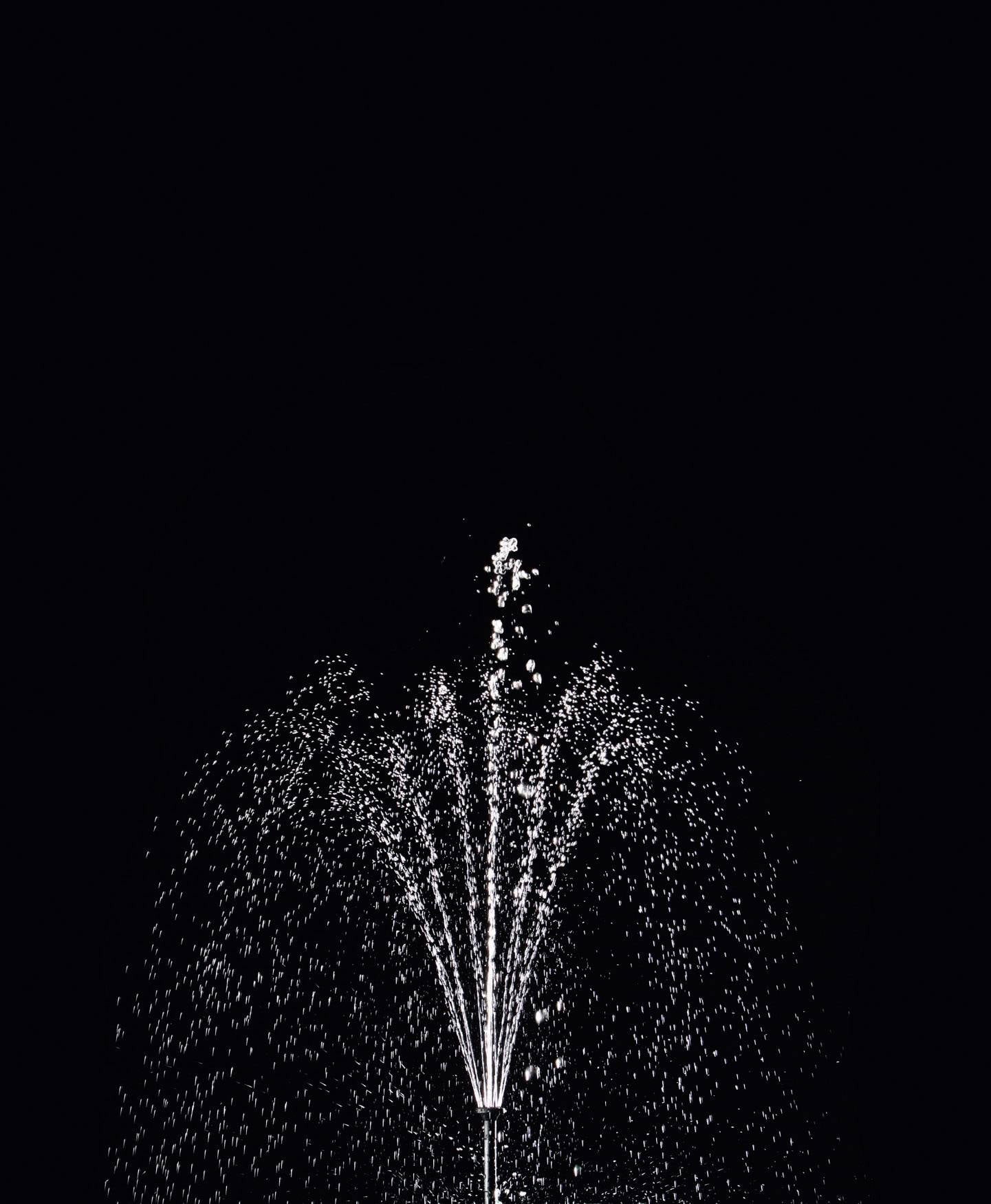 Wasserfontäne sprüht bei Nacht in die Höhe, schwarzer Hintergrund.