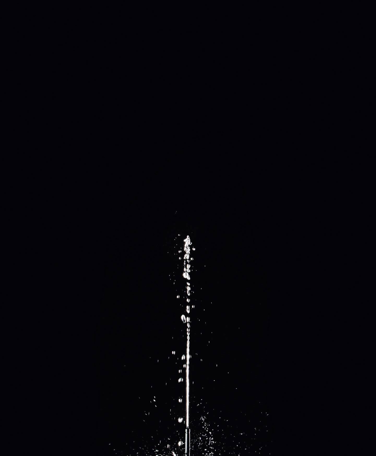 Ein Wasserstrahl spritzt senkrecht in die Luft vor einem schwarzen Hintergrund.