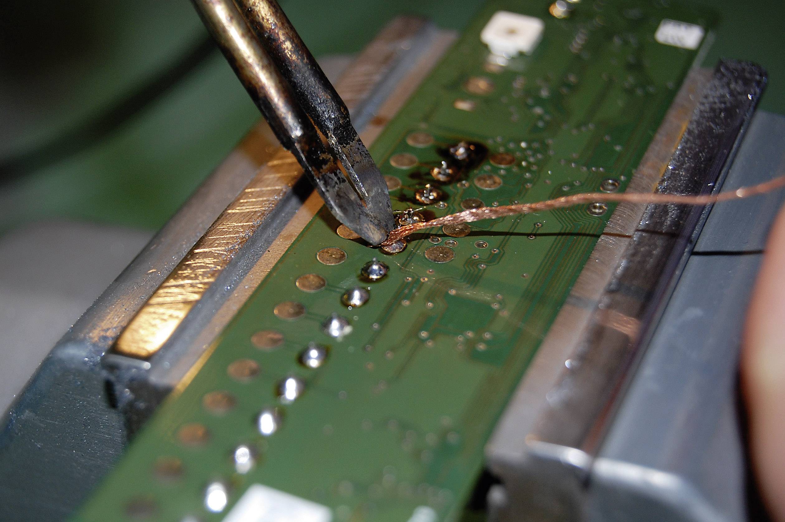 Lötvorgang an einer grünen Leiterplatte mit Lötkolben. Kupferdraht wird erhitzt und verbunden. Aufnahme zeigt Präzisionsarbeit.