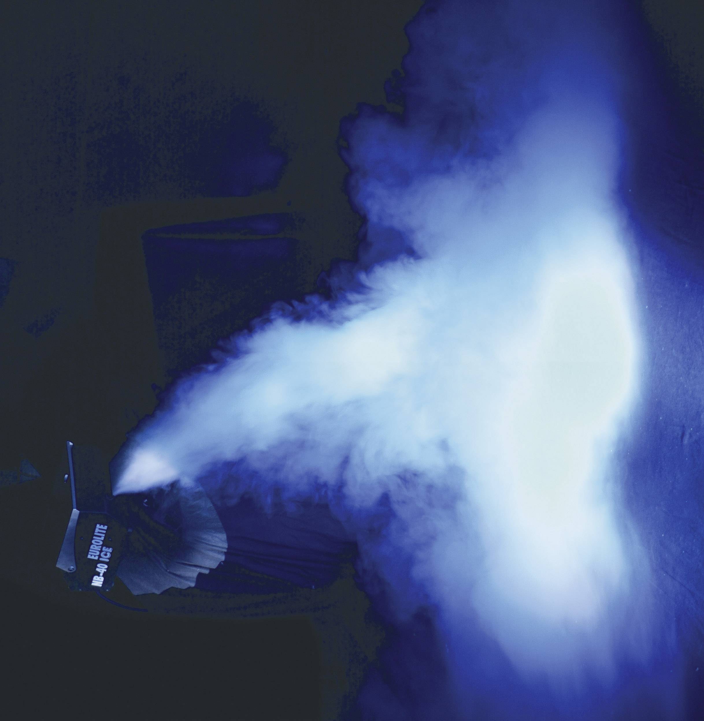 Eine Nebelmaschine erzeugt einen leuchtend blauen Nebelstrahl auf einer dunklen Bühne.