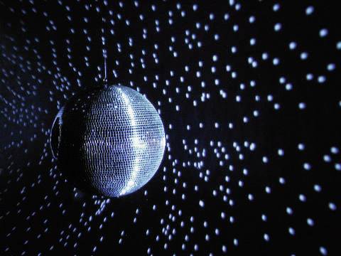 Eine Discokugel dreht sich, reflektiert Lichtpunkte an Wänden und Decke. Die Punkte erzeugen ein dynamisches Muster im Dunkeln.