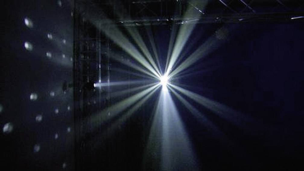Ein heller Scheinwerfer strahlt mehrere Lichtstrahlen in einem dunklen Raum aus und erzeugt ein magisches Lichtspiel an den Wänden.