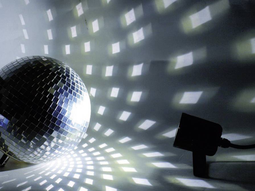 Eine Discokugel reflektiert Lichtmuster an Wände und Boden in einem dunklen Raum, während ein Scheinwerfer sie anstrahlt.