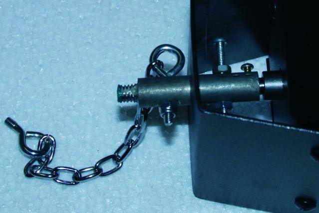 Ein Metallstift mit angehängter Kette ist an einem schwarzen Gehäuse montiert, vermutlich Teil eines mechanischen oder elektronischen Geräts.