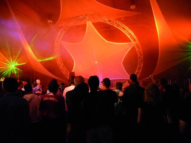 Menschenmenge bei einem Konzert mit bunten Lichtern und einer großen, sternförmigen Dekoration im Hintergrund.