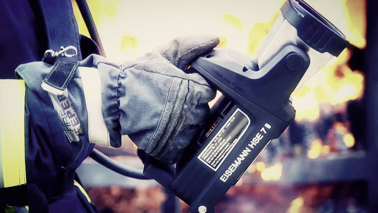 Ein Feuerwehrmann hält ein Hochleistungslöschgerät vor einem brennenden Hintergrund. Aufmerksamkeit auf die Ausrüstung.