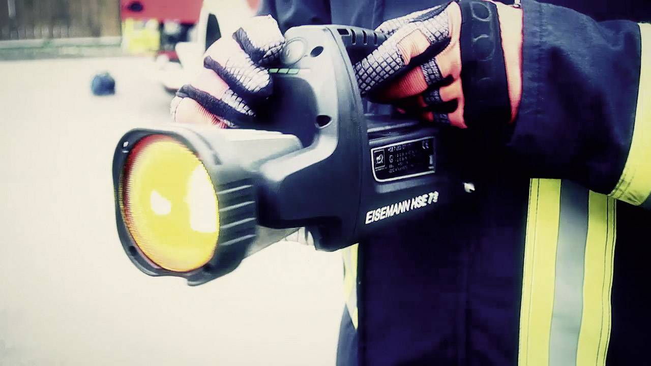 Eine Person in Feuerwehrkleidung hält eine große, orange Taschenlampe. Die Marke 'EISEMANN HSE 27' ist sichtbar.