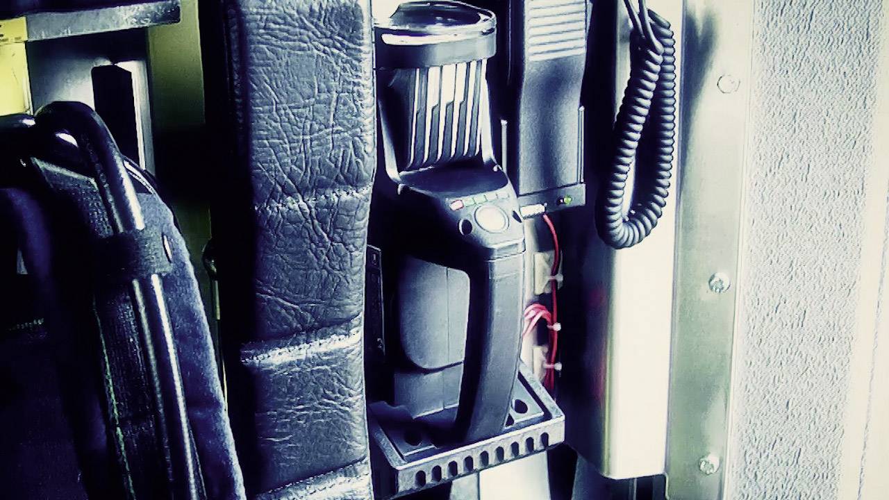 Ein Funkgerät ist in einem Halter an einer Wand montiert, umgeben von Kabeln und einer schwarzen Tasche.