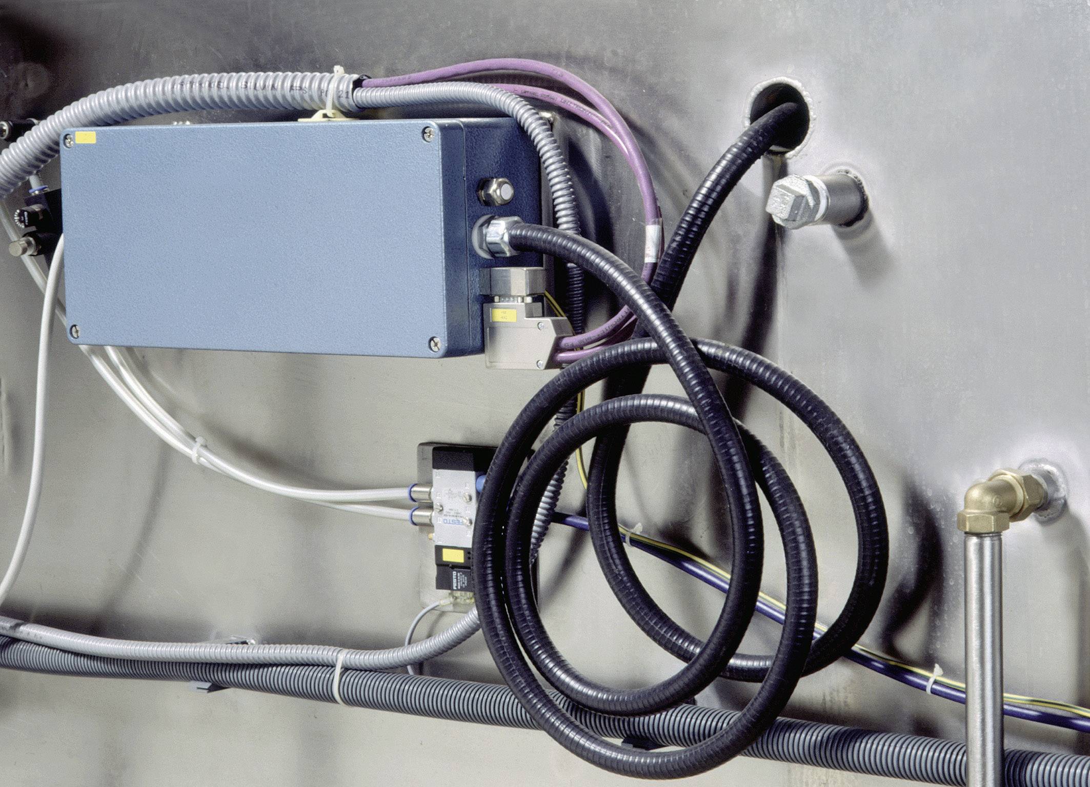 Ein elektrischer Schaltschrank mit verschiedenen Kabeln und Rohren, die in beide Richtungen verlaufen, vor einer Metallwand.