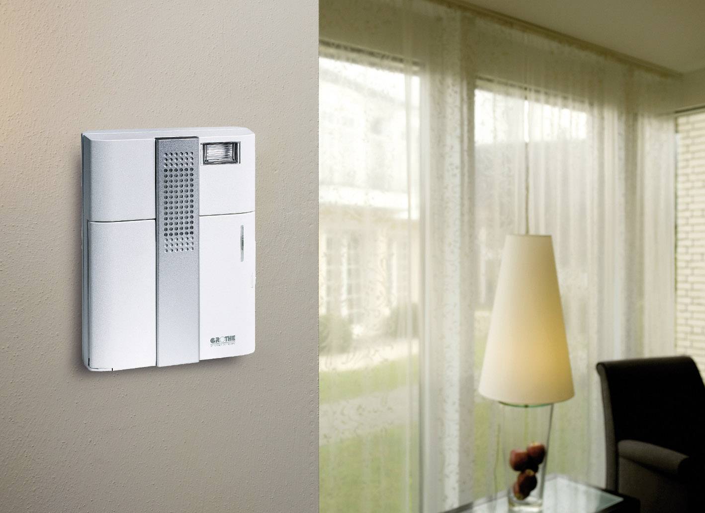 Ein modernes Intercom-System an der Wand eines Wohnzimmers, mit einem Fenster im Hintergrund, das den Raum erhellt.