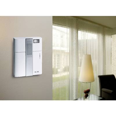 Ein modernes Intercom-System an der Wand eines Wohnzimmers, mit einem Fenster im Hintergrund, das den Raum erhellt.