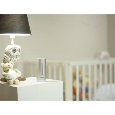Ein Kinderzimmer mit einem Nachttisch, auf dem eine Lampe mit Eulenfigur, ein Stoffteddy und ein digitales Gerät stehen; im Hintergrund ein Babybett.