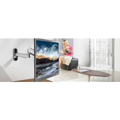 Eine Person sitzt auf einem Sessel in einem modernen Wohnzimmer und liest ein Magazin. An der Wand hängt ein Flachbildschirm mit einer Landschaftsszene.