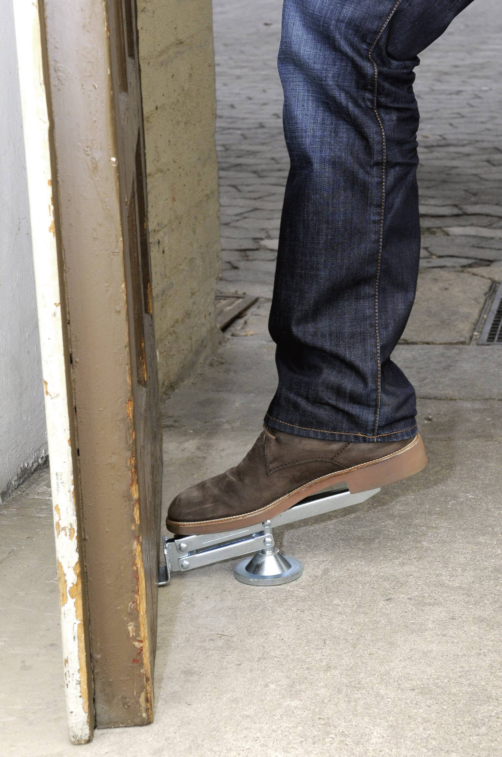Eine Person in Jeans öffnet eine Tür mit einem Fußmechanismus, um Kontakt mit der Hand zu vermeiden.