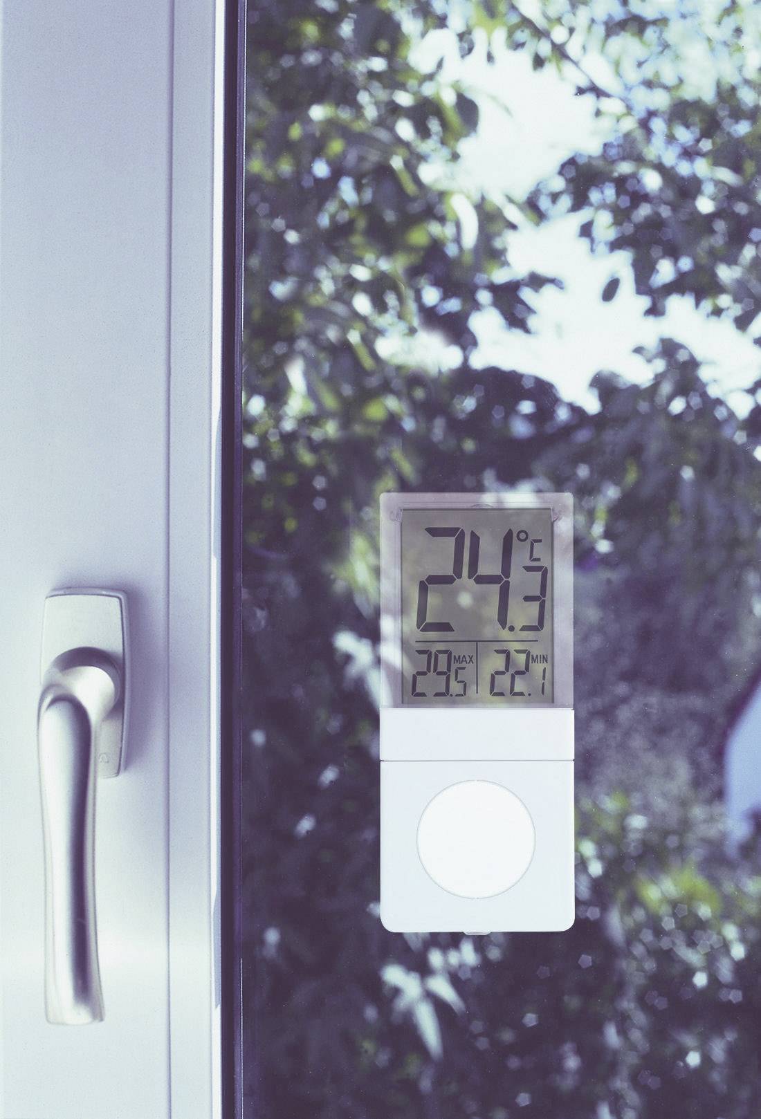 Ein Thermometer zeigt 24°C an einem sonnigen Tag. Es ist an einem Fenster angebracht, durch das grüne Bäume zu sehen sind.