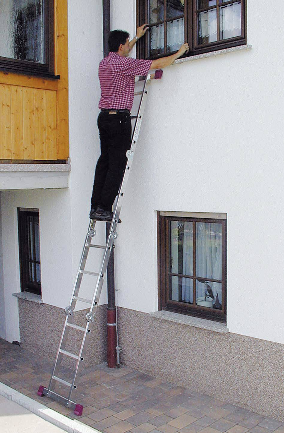 Ein Mann steht auf einer Leiter und reinigt ein Fenster an einem Haus aus weißem Putz mit Holzelementen.