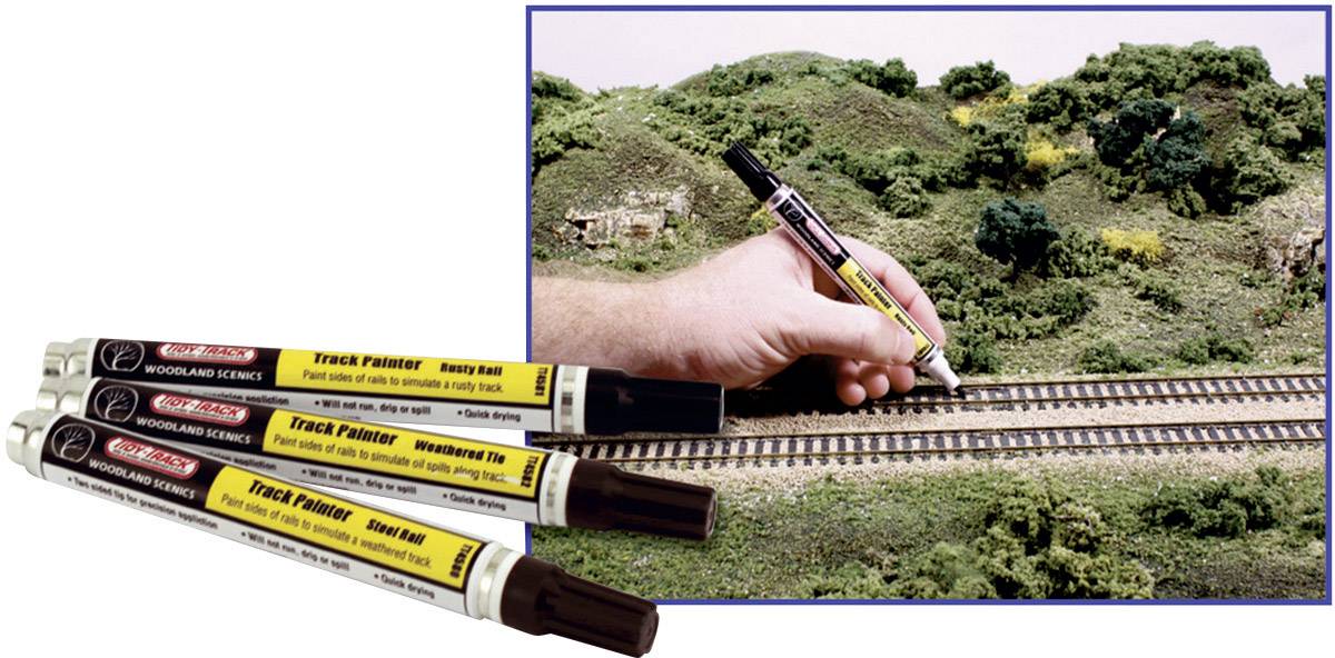 'Eine Hand bemalt Schienen auf einer Miniatureisenbahnlandschaft mit einem Spezialmarker. Drei Marker liegen im Vordergrund.'
