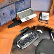 Ein Büroarbeitsplatz mit zwei Monitoren, einem Laptop, einem Telefon und einer Computertastatur auf einem hölzernen Schreibtisch.