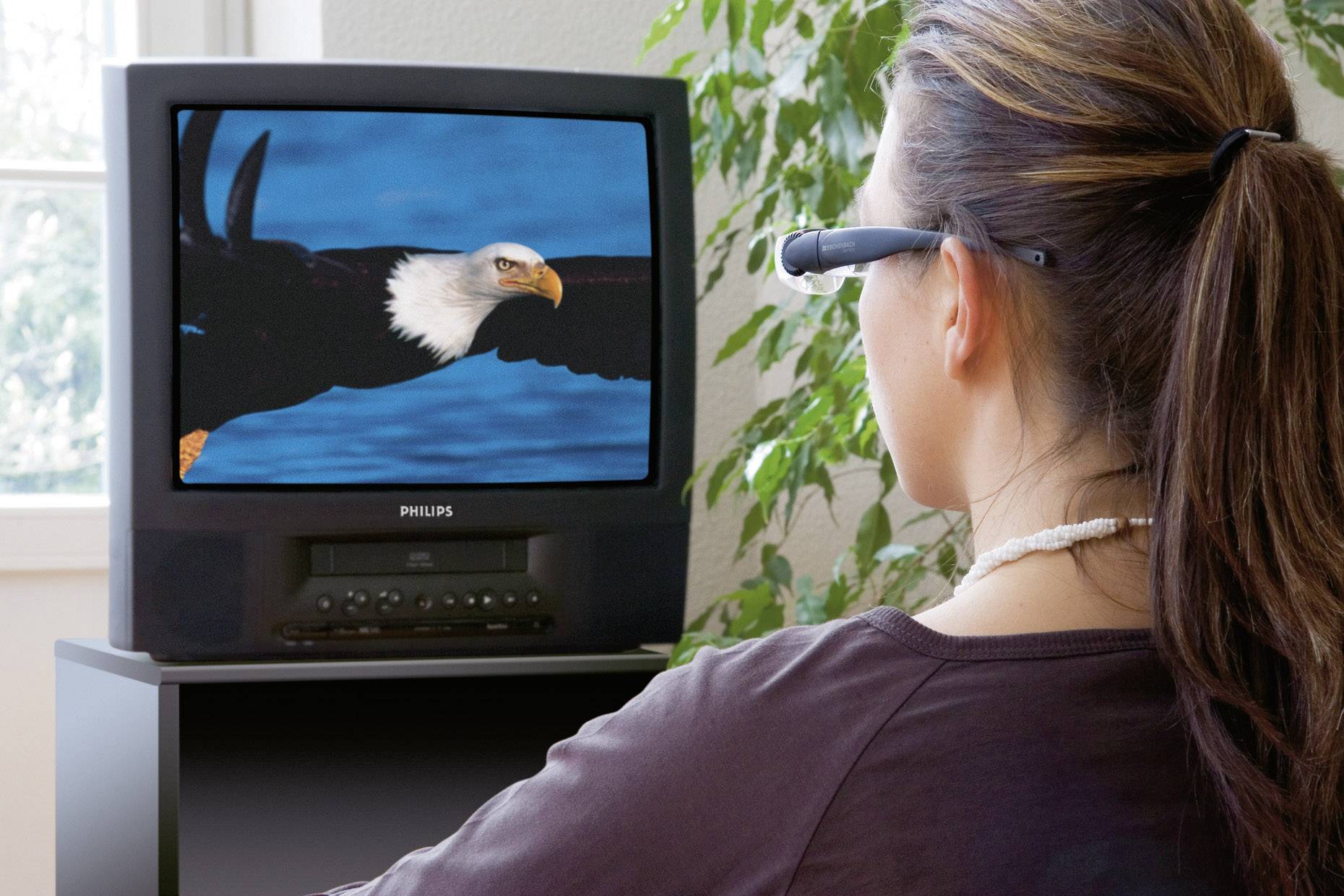 Eine Frau trägt 3D-Brille und schaut auf einen Fernseher, der einen fliegenden Weißkopfseeadler zeigt.