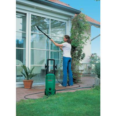 Eine Frau reinigt Fenster mit einem Hochdruckreiniger in einem Gartenbereich. Im Hintergrund sind Pflanzen und ein Haus zu sehen.