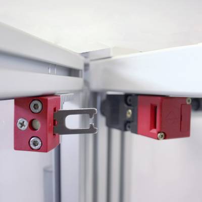 Ein roter Schaltersensor ist an einer Metallkante montiert. Er dient zur Sicherheitsüberwachung von Maschinenbewegungen.