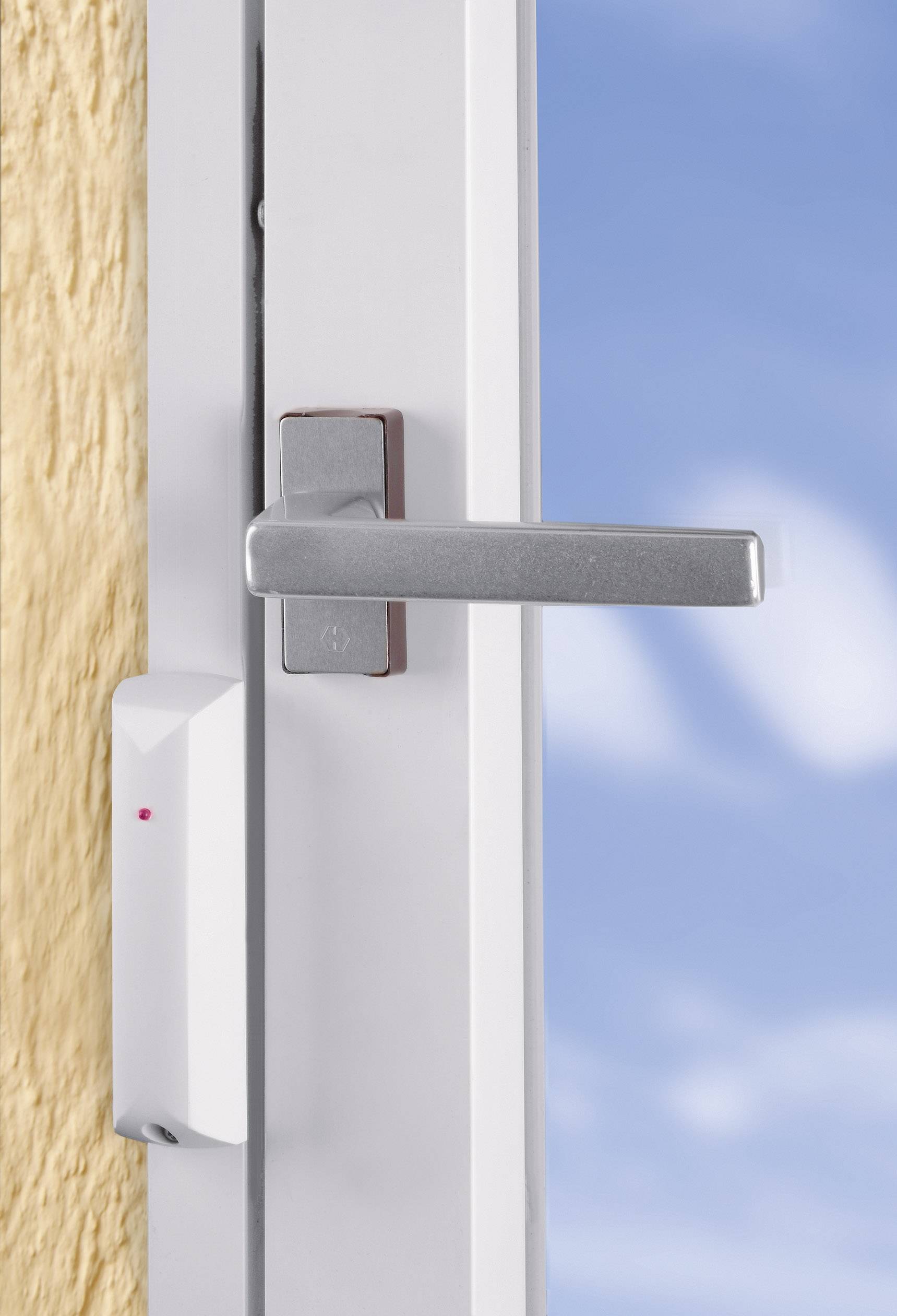 Ein geöffnetes Fenster mit einem silbernen Griff, das nach draußen zeigt. Ein Sensor ist am Rahmen angebracht, und der Himmel ist blau.