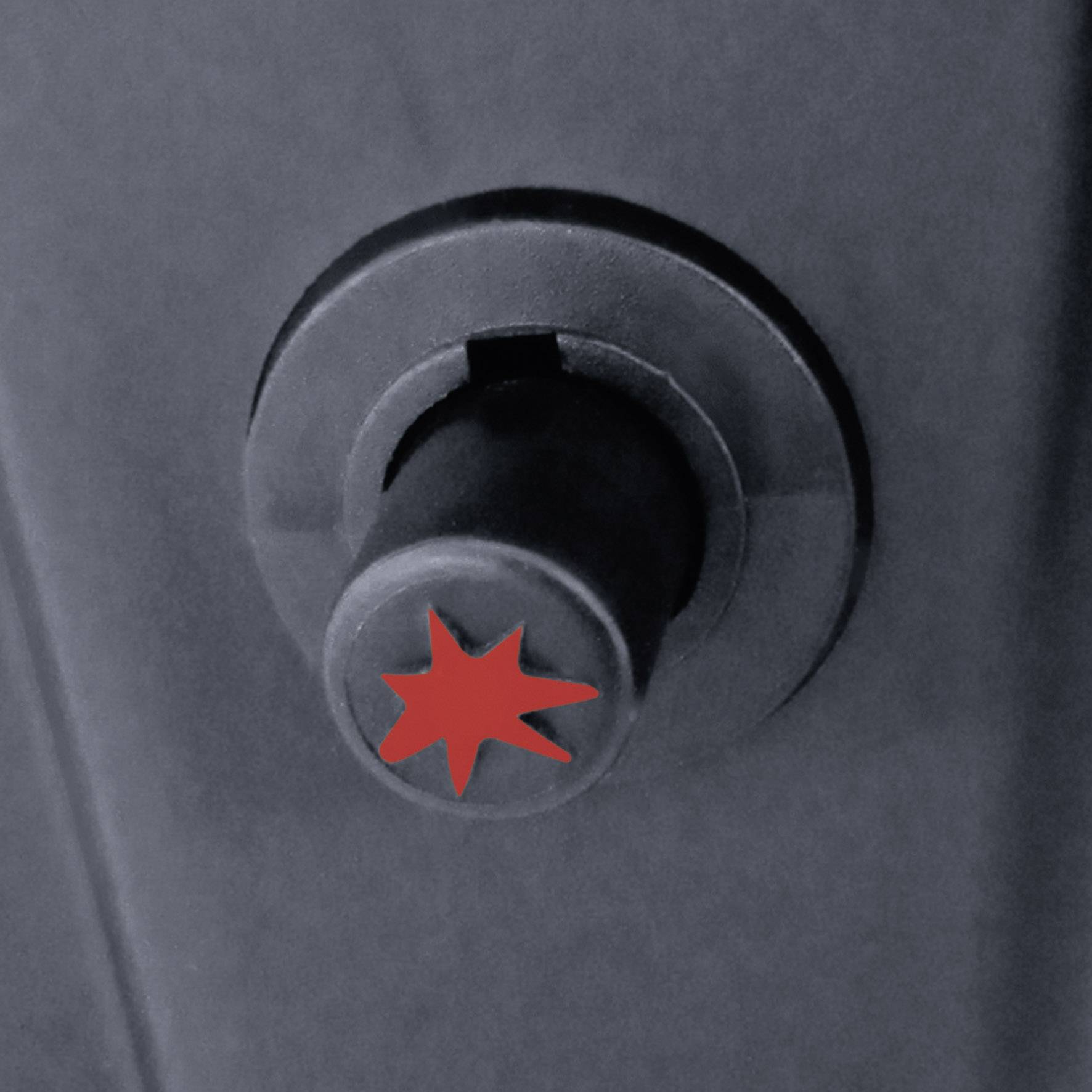 Ein grauer Metallknopf mit einem roten Sternsymbol in der Mitte, auf einer dunkelgrauen Oberfläche montiert.
