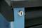 Nahaufnahme eines Schlüssellochs in einem blauen Metallschrank, teilweise verdeckt. Der Schrank hat eine schwarze Oberfläche.