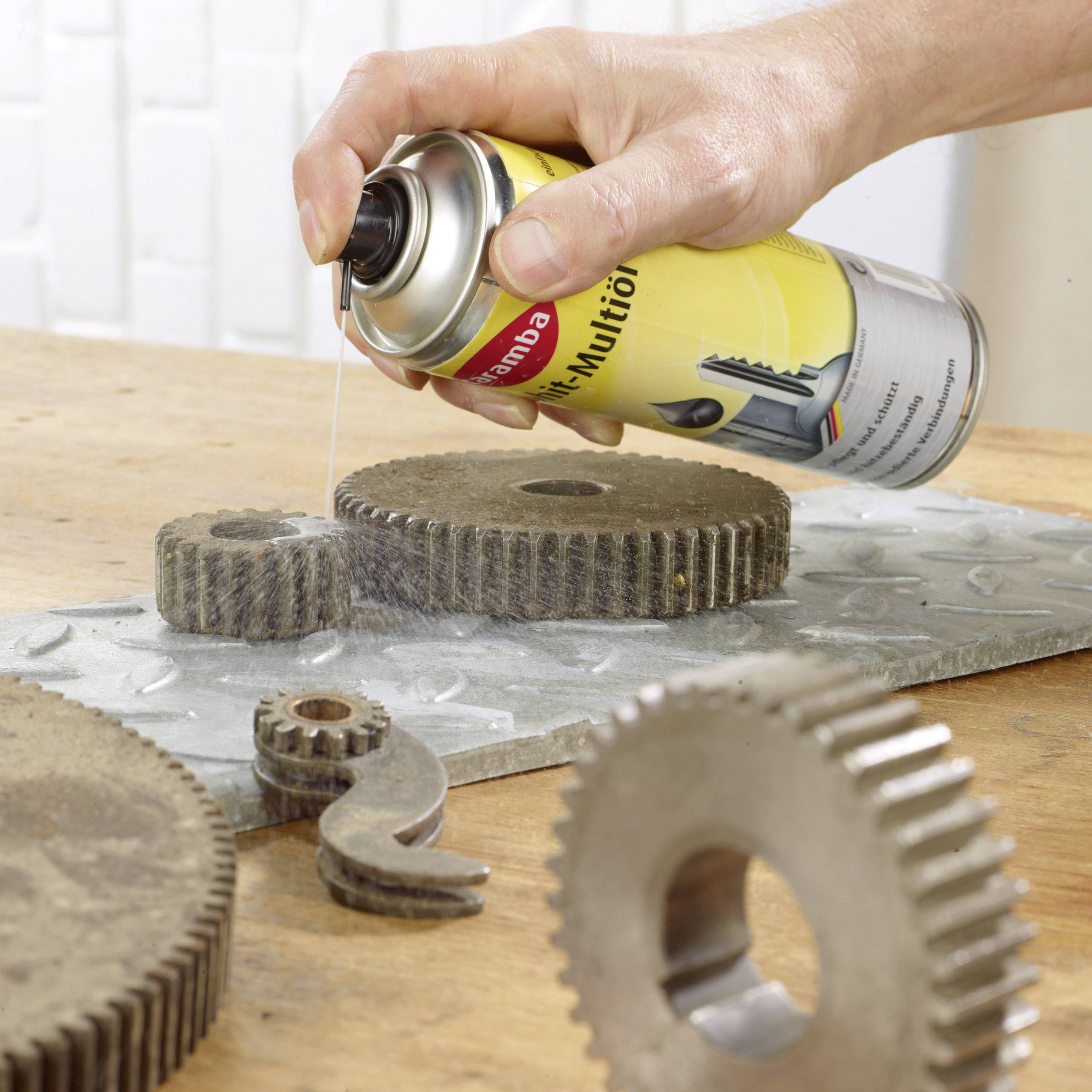 Eine Hand sprüht Schmiermittel auf Zahnradteile auf einem Tisch, um Reibung zu reduzieren und die Funktionalität zu erhöhen.