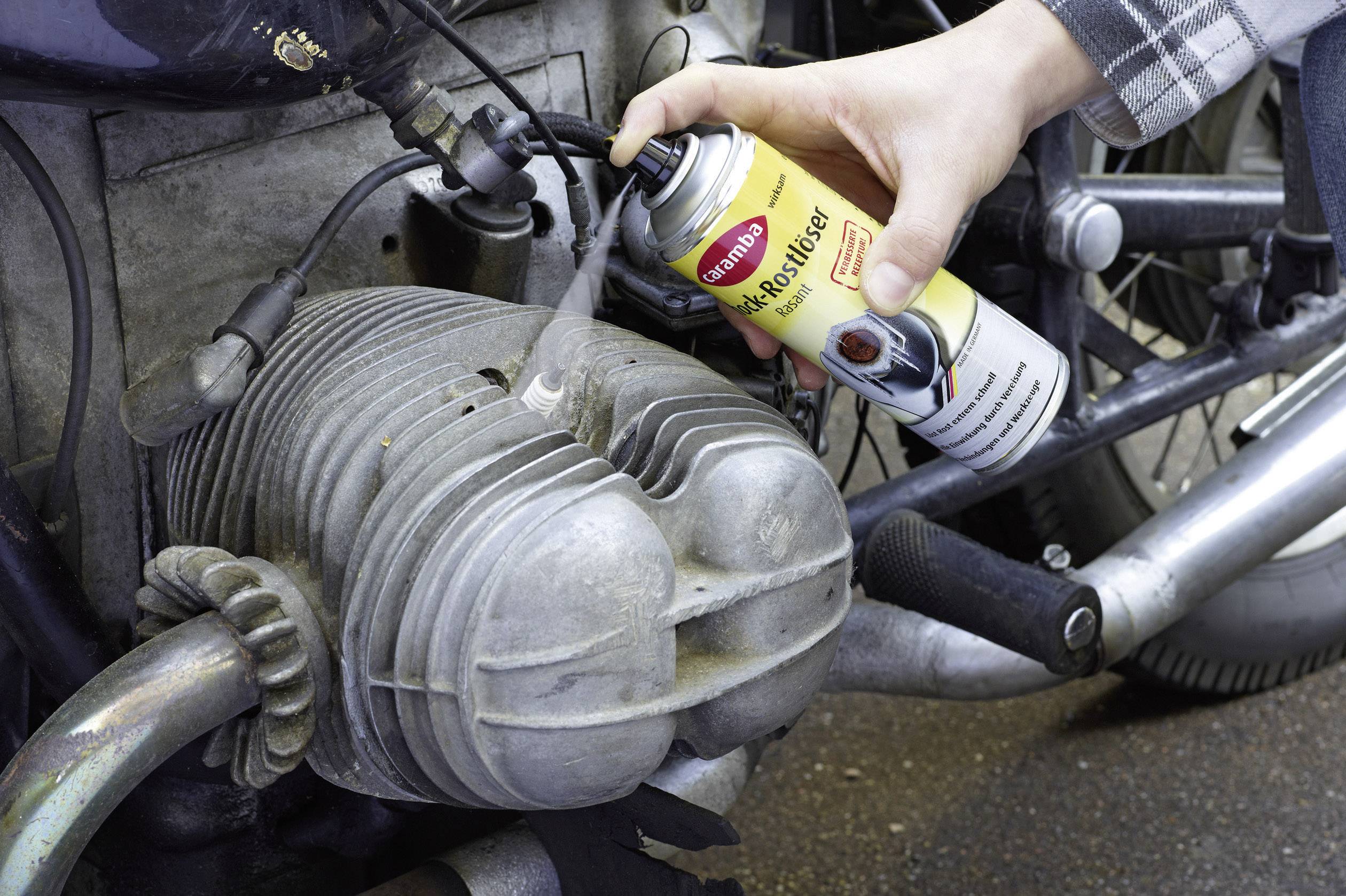 'Hand reinigt Motorradteil mit Motorspray aus einer Dose'