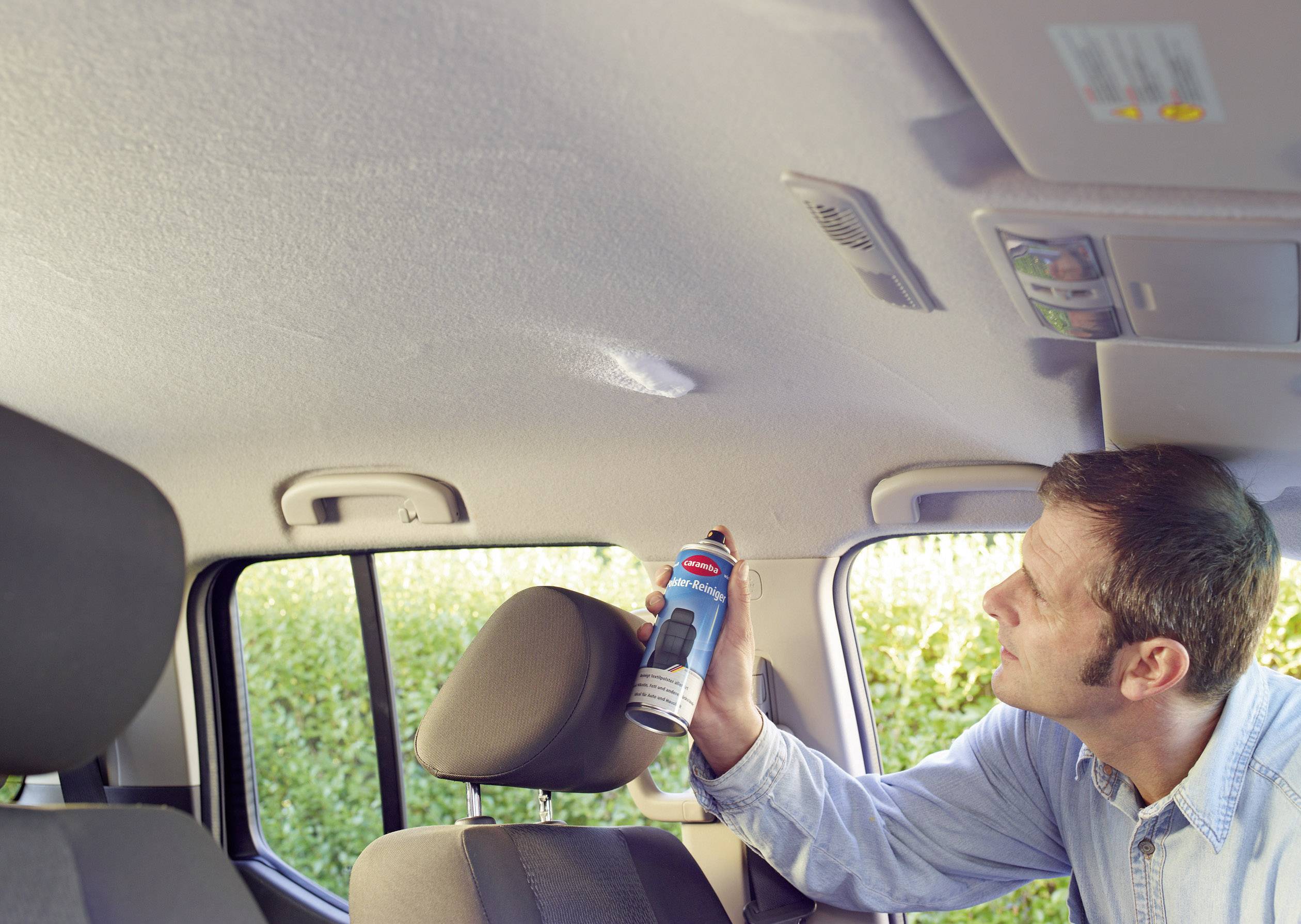 Ein Mann benutzt eine Sprühdose, um den Innenhimmel eines Autos zu reinigen. Er konzentriert sich auf einen bestimmten Bereich.