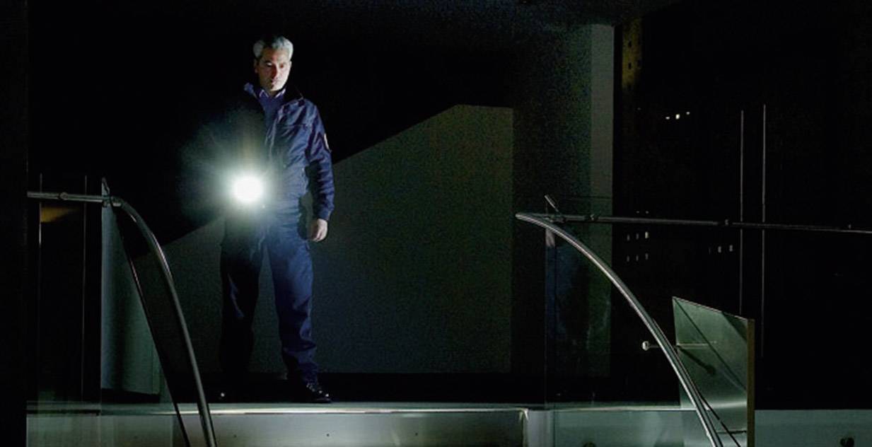 Eine Person steht in dunkler Umgebung auf einer Treppe und hält eine leuchtende Taschenlampe, die den Weg erhellt.