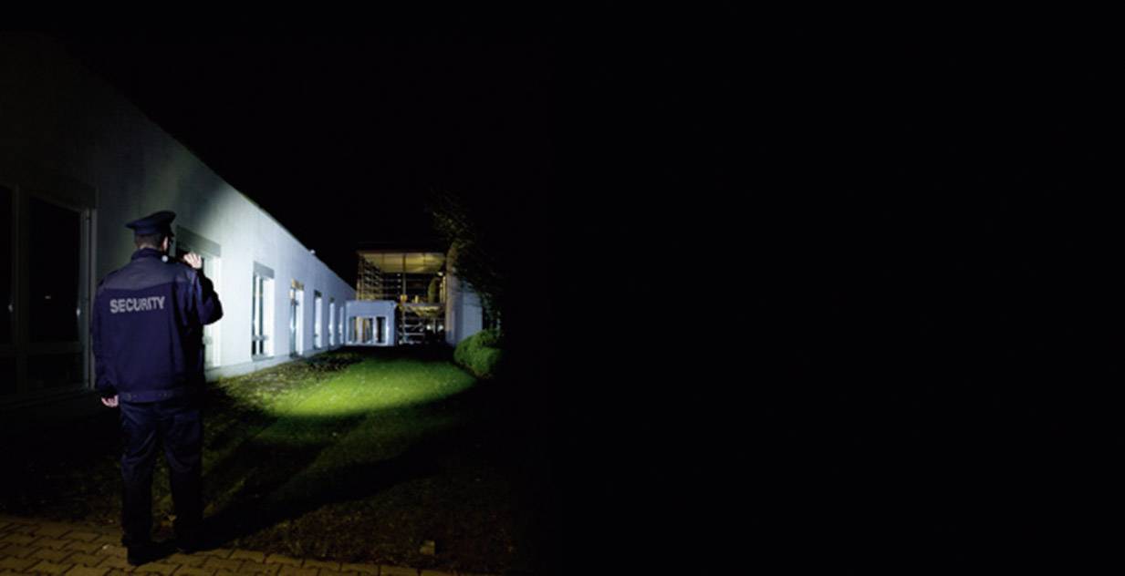 Ein Sicherheitsbeamter im Dunkeln leuchtet mit einer Taschenlampe auf ein Gebäude.
