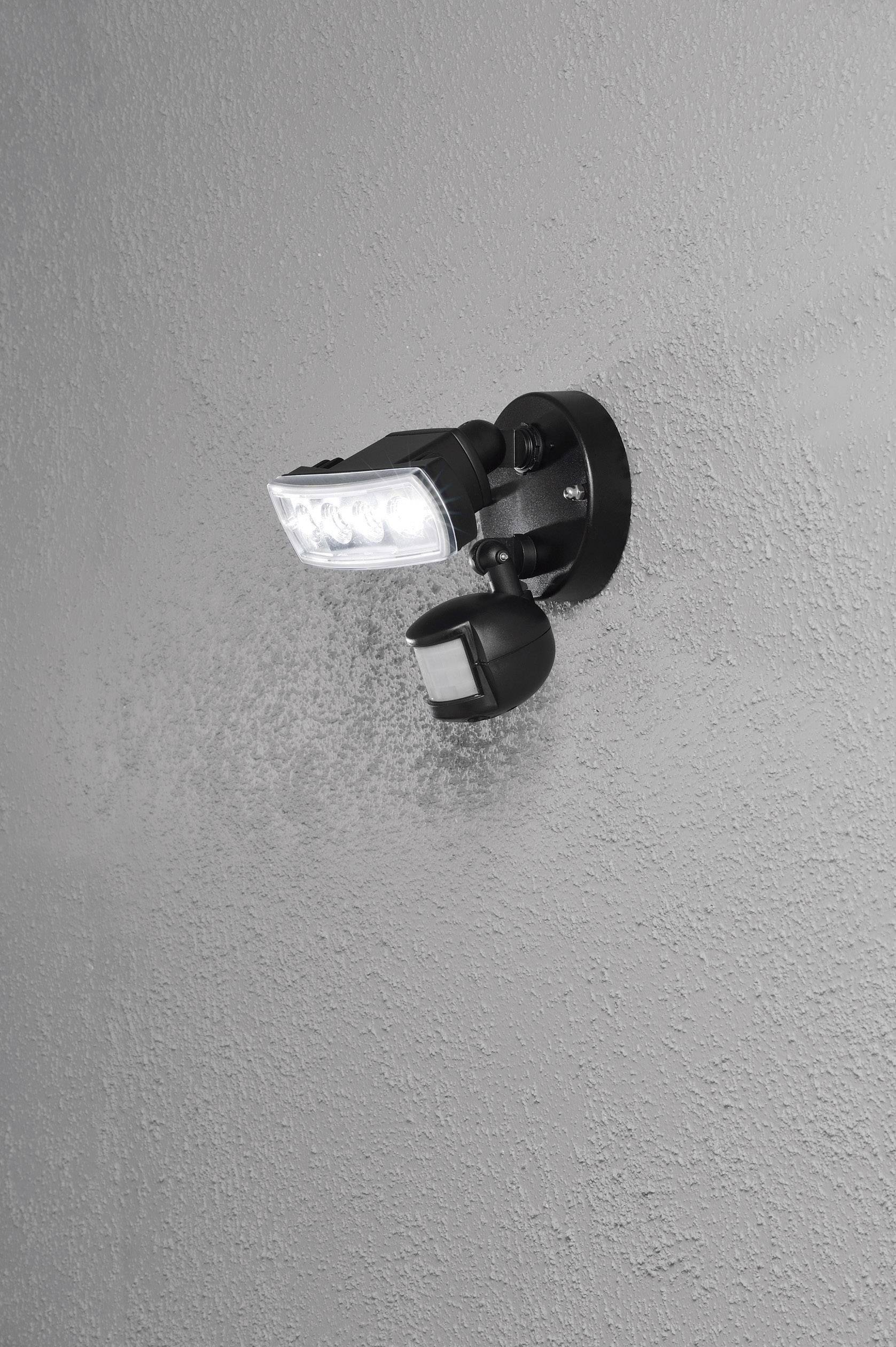 Außenleuchte mit Bewegungssensor an grauer Wand montiert, leuchtet weißes Licht.