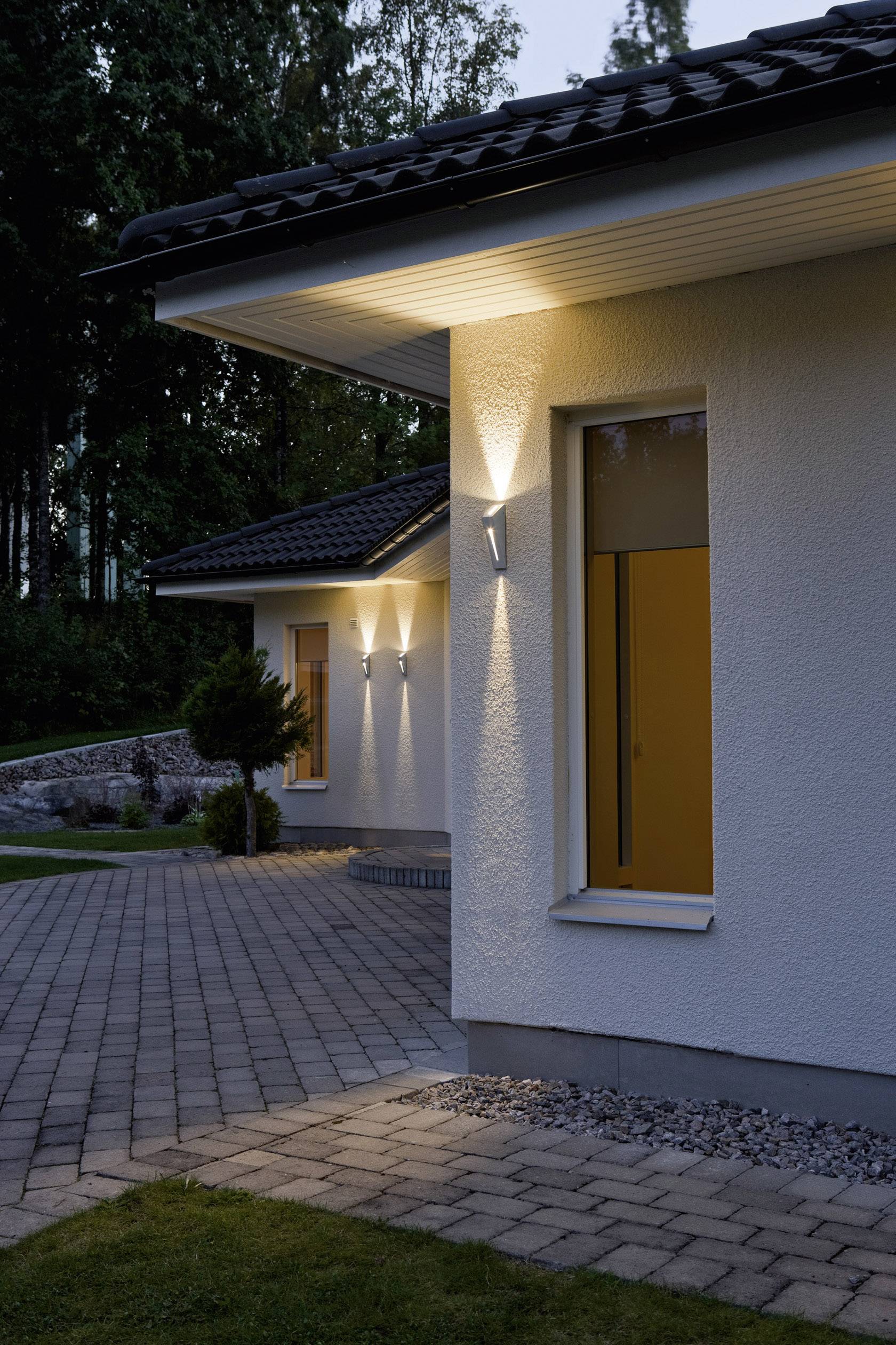 Ein zeitgenössisches Haus mit heller Außenbeleuchtung in der Dämmerung, umgeben von Bäumen und einem Weg aus Pflastersteinen.